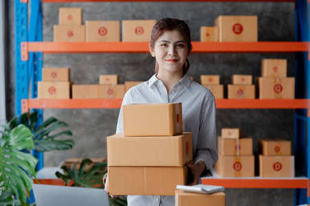 A beautiful Asian business owner opens an online store, she is checking orders from customers, sending goods through a courier company, concept of a woman opening an online business.の写真素材