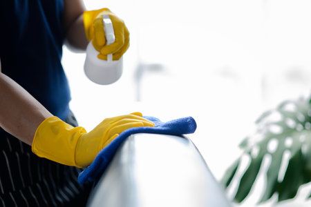 Person cleaning the room, cleaning staff is using cloth and spraying disinfectant to wipe the sofas in the company office room. Cleaning staff. Maintaining cleanliness in the organization.の写真素材
