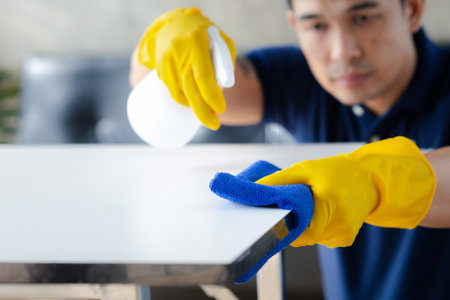 Person cleaning the room, cleaning staff is using cloth and spraying disinfectant to wipe the tables in the company office room. Cleaning staff. Maintaining cleanliness in the organization.の写真素材
