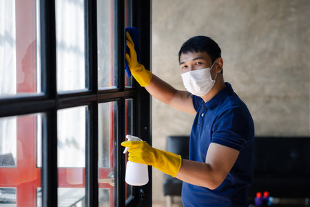 Person cleaning the room, cleaning staff is using cloth and spraying disinfectant to wipe the glass in the company office room. Cleaning staff. Concept of cleanliness in the organization.の写真素材