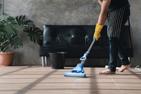 Person cleaning the room, the cleaning worker is using a mop to clean the floor of the living room in the company office. Cleaning staff. Maintaining cleanliness in the organization.の写真素材