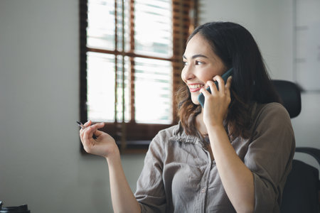 Asian woman talking on the phone, she is a salesperson in a startup company, she is calling customers to sell products and promotions. Concept of selling products through telephone channels.の写真素材