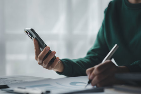 Business man looking at financial information from a mobile phone, he is checking company financial documents, he is an executive of a startup company. Concept of financial management.の写真素材