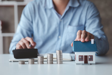 People with house models and piles of coins are calculating and recording income and expenses for financial planning, financial planning ideas for home and real estate purchases.の写真素材