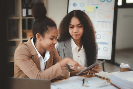 Two American women are working together in the office of a startup company. They are having a brainstorming and planning meeting in a joint department, women leading the way. Concept of women's work.の写真素材