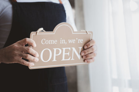 Man holding open/close sign in front of entrance, Goods and Service shop clerk holding sign to...