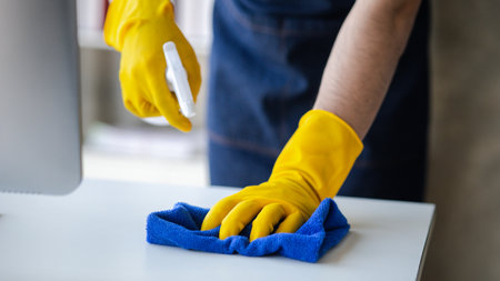 Person cleaning the room, cleaning staff is using cloth and spraying disinfectant to wipe the glass...