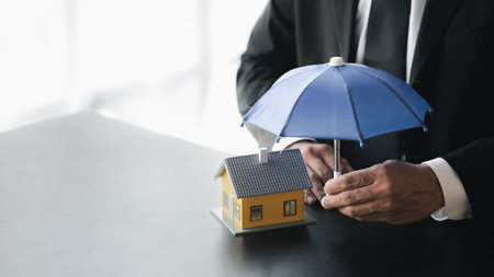 Individuals holding small umbrellas and model homes, housing insurance against impending loss and fire, building fire insurance, home and real estate insurance concepts.の写真素材