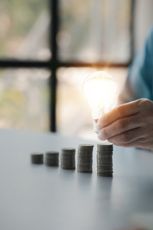 Businessman holds a glowing light bulb on top of the highest pile of coins, Placing coins in a row...