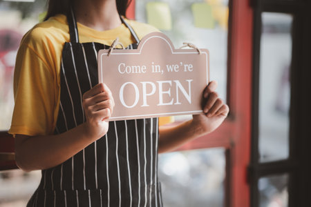 Woman holding open/close sign in front of entrance, Goods and Service shop clerk holding sign to...