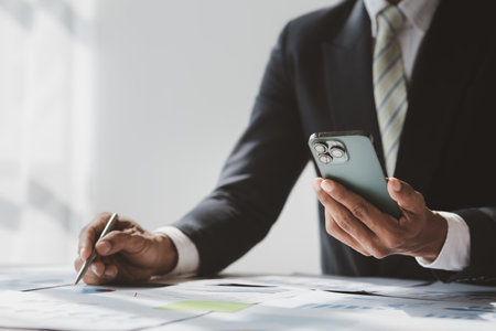 Business man looking at financial information from a mobile phone, he is checking company financial documents, he is an executive of a startup company. Concept of financial management.の写真素材