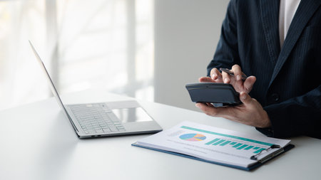 Business man using a calculator to calculate numbers on a company's financial documents, he is analyzing historical financial data to plan how to grow the company. Financial concept.の写真素材
