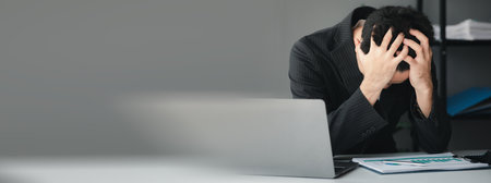 Businessman sitting in a company office, he is holding his head having a severe headache due to long...