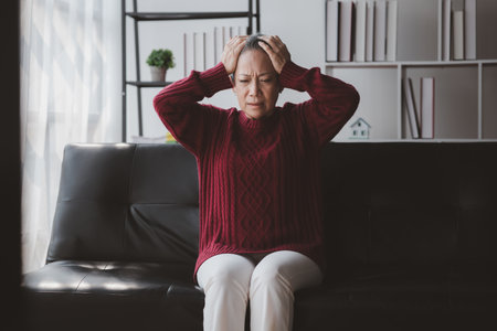 Senior woman sitting in the living room at home and showing body aches, aging sickness, body aches of elderly people, organ degeneration.の写真素材