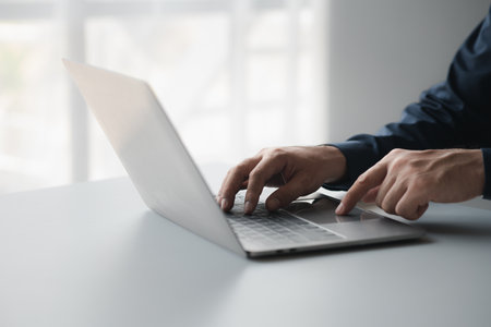 Person typing on a laptop keyboard, businessman is working in a startup company's office, he is...