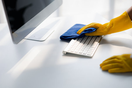 Person cleaning room, cleaning worker is using cloth to wipe computer keyboard in company office room. Cleaning staff. Concept of cleanliness in the organization.の写真素材