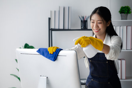 Person cleaning room, cleaning worker is using cloth to wipe computer screen in company office room. Cleaning staff. Concept of cleanliness in the organization.の写真素材