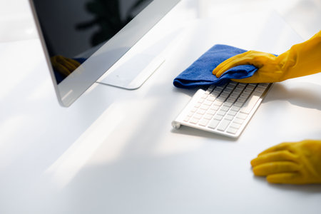 Person cleaning room, cleaning worker is using cloth to wipe computer keyboard in company office room. Cleaning staff. Concept of cleanliness in the organization.の写真素材