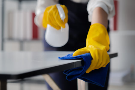 Person cleaning the room, cleaning staff is using cloth and spraying disinfectant to wipe the desk in the company office room. Cleaning staff. Maintaining cleanliness in the organization.の写真素材