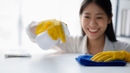 Person cleaning the room, cleaning staff is using cloth and spraying disinfectant to wipe the desk in the company office room. Cleaning staff. Maintaining cleanliness in the organization.の写真素材