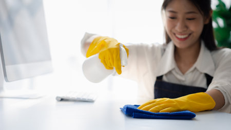 Person cleaning the room, cleaning staff is using cloth and spraying disinfectant to wipe the desk in the company office room. Cleaning staff. Maintaining cleanliness in the organization.の写真素材