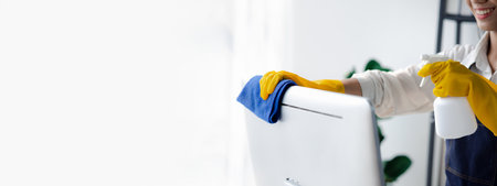 Person cleaning room, cleaning worker is using cloth to wipe computer screen in company office room. Cleaning staff. Concept of cleanliness in the organization.の写真素材
