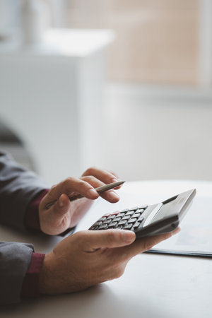 Businessman using a calculator to calculate numbers on a company's financial documents, he is analyzing historical financial data to plan how to grow the company. Financial concept.の写真素材