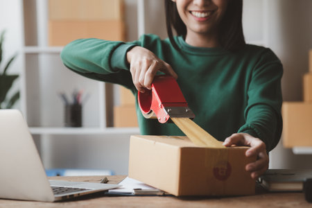 A person is packing parcel boxes according to orders, she owns an online store, she packs and ships through a private transport company. Online selling and online shopping concepts.の写真素材
