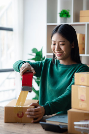 A person is packing parcel boxes according to orders, she owns an online store, she packs and ships...