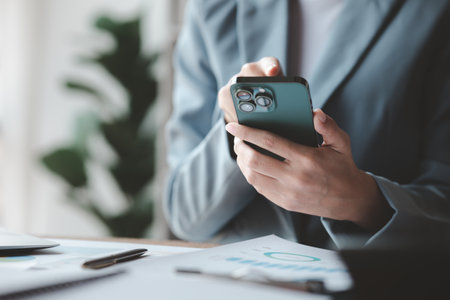 Beautiful Asian woman playing mobile phone in her break from work, she is a marketing manager of a startup company, female leader, supervisor, ceo. Female Leadership Concept.の写真素材