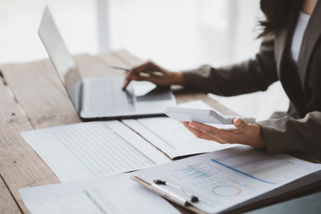 Businessman using a calculator to calculate numbers on a company's financial documents, she is analyzing historical financial data to plan how to grow the company. Financial concept.の写真素材