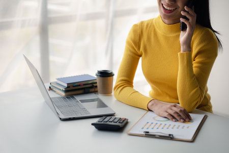 Asian woman talking on the phone, she is a salesperson in a startup company, she is calling customers to sell products and promotions. Concept of selling products through telephone channels.の写真素材