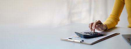 Businessman using a calculator to calculate numbers on a company's financial documents, she is...