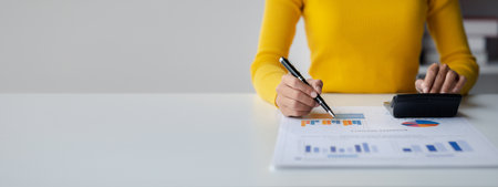 Businessman using a calculator to calculate numbers on a company's financial documents, she is...