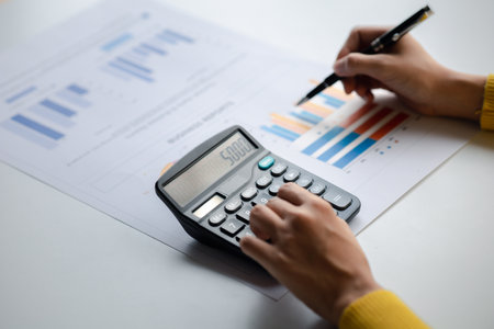 Businessman using a calculator to calculate numbers on a company's financial documents, she is...