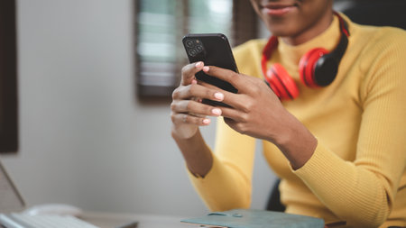 A young American woman is a start-up businesswoman, she sits in the office and uses mobile phones, manages and runs her business from a young generation. Startup business management concept.の写真素材