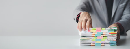 Person with stacks of company financial report papers in office, company employee picking up papers on table to use for performance summary and filing. Document management concept.の写真素材