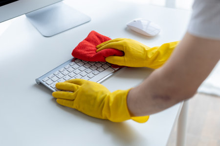 Person cleaning room, cleaning worker is using cloth to wipe computer keyboard in company office...