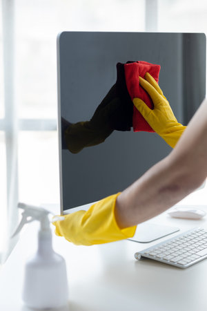 Person cleaning room, cleaning worker is using cloth to wipe computer screen in company office room. Cleaning staff. Concept of cleanliness in the organization.の写真素材