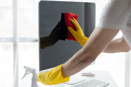 Person cleaning room, cleaning worker is using cloth to wipe computer screen in company office room. Cleaning staff. Concept of cleanliness in the organization.の写真素材