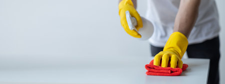 Person cleaning the room, cleaning staff is using cloth and spraying disinfectant to wipe the table...