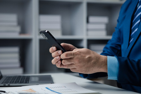 Business man looking at financial information from a mobile phone, he is checking company financial documents, he is an executive of a startup company. Concept of financial management.の写真素材