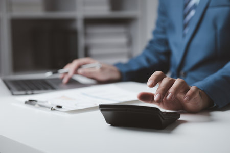 Businessman using a calculator to calculate numbers on a company's financial documents, he is analyzing historical financial data to plan how to grow the company. Financial concept.の写真素材