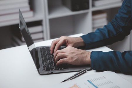Person typing on laptop keyboard, businessman working on laptop, he is typing messages to colleagues and making financial information sheet to sum up the meeting.の写真素材