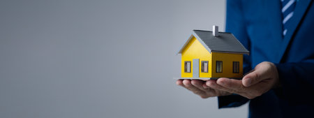 Person puts her hand on top of a miniature house model, photo of home insurance concept, when buying a new home should have home insurance to be sure if there is any danger to the home.の写真素材