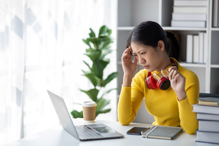 Teenage woman sitting in white room with laptop, she has stress, she is a student studying online with laptop at home, university student studying online, online web education concept.の写真素材