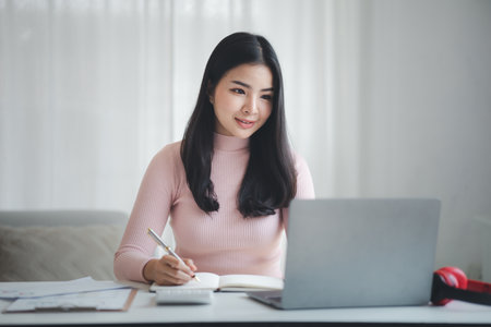 A beautiful Asian businesswoman sitting in her private office, she is checking company financial documents, she is a female executive of a startup company. Concept of financial management.の写真素材