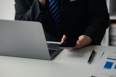 Business man looking at financial information from a mobile phone, he is checking company financial documents, he is an executive of a startup company. Concept of financial management.の写真素材