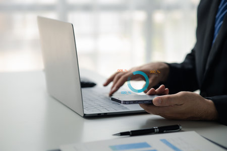 Businessman holding mobile phone with hologram graph showing financial data for calculation, he is analyzing historical financial data to plan how to grow the company. Financial concept.の写真素材