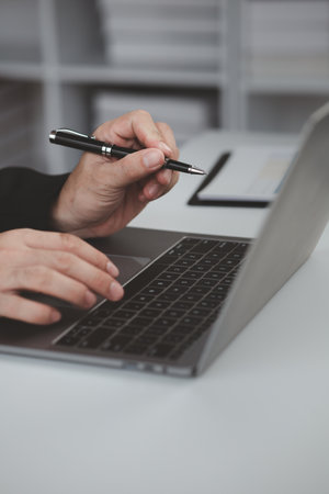 Person typing on laptop keyboard, businessman working on laptop, he is typing messages to colleagues and making financial information sheet to sum up the meeting.の写真素材